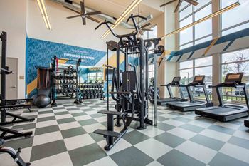 A gym with weights and cardio equipment in a building with large windows
